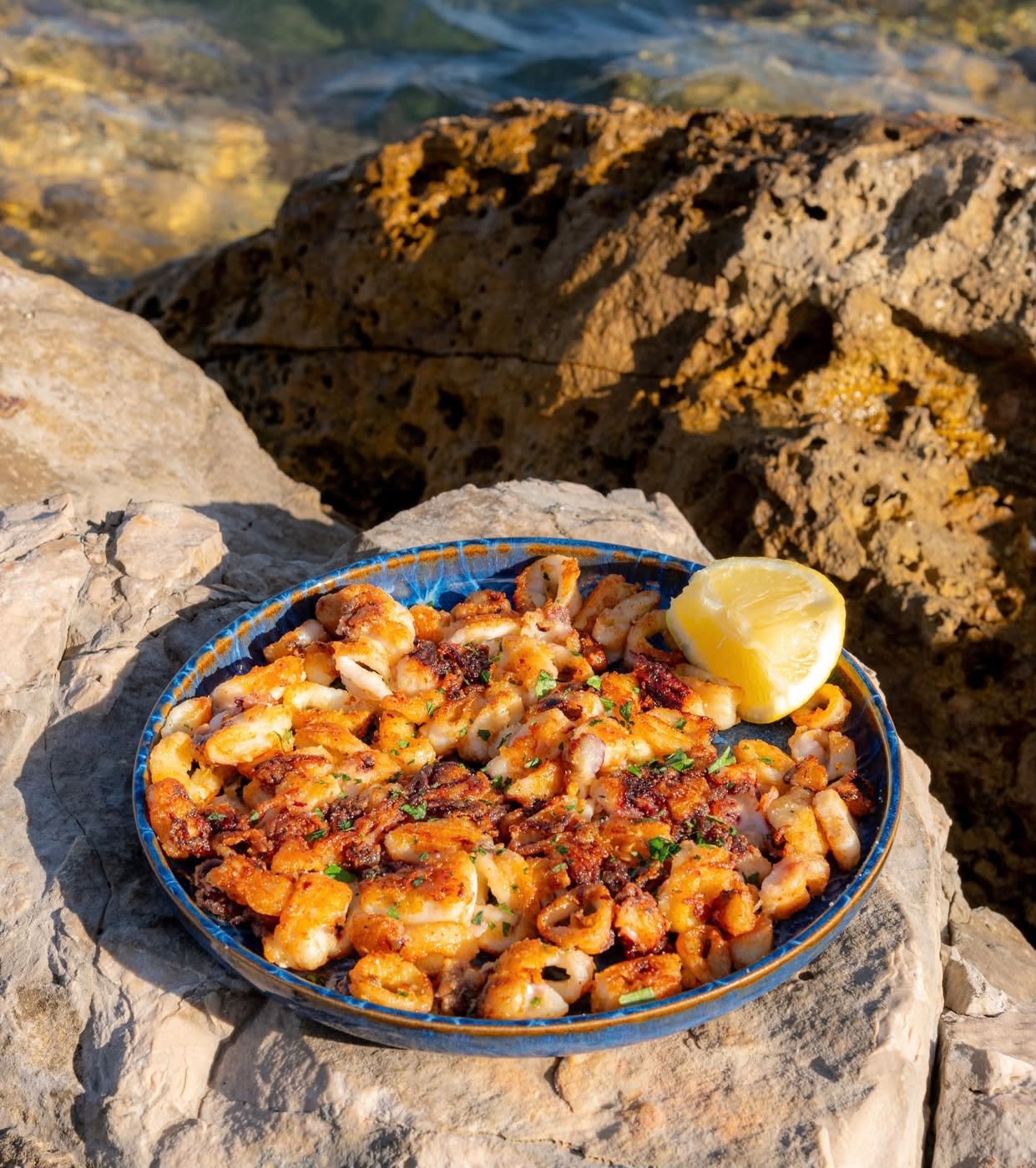 Calamari fritti con limone, serviti sugli scogli davanti al mare
