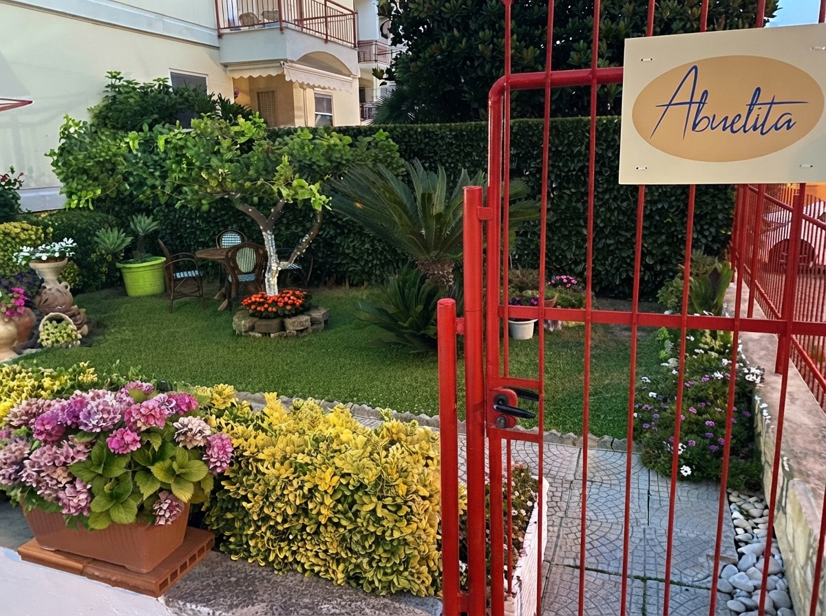 La entrada de Abuelita: la verja roja con el letrero y el jardín florido