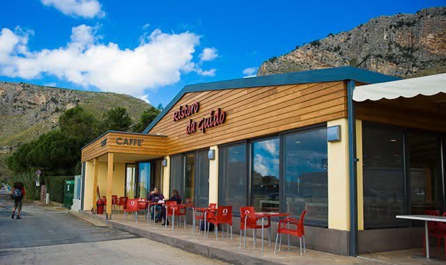 Il Ristoro da Guido: locale in legno con tavolini rossi all'aperto e la montagna sullo sfondo